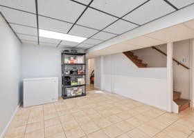 Spacious basement featuring tiled floor, storage shelves, and staircase in a modern setting.