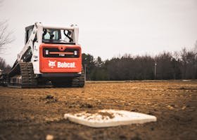 A skid loader working on maintaining a baseball field under construction.