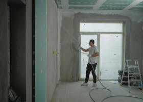 A man sprays paint on a wall while renovating an indoor room with professional equipment.